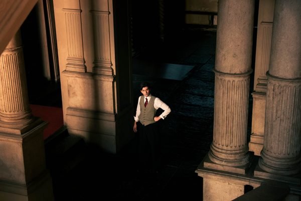 Un illusionista fermo fra le colonne di un cortile, nella luce radente