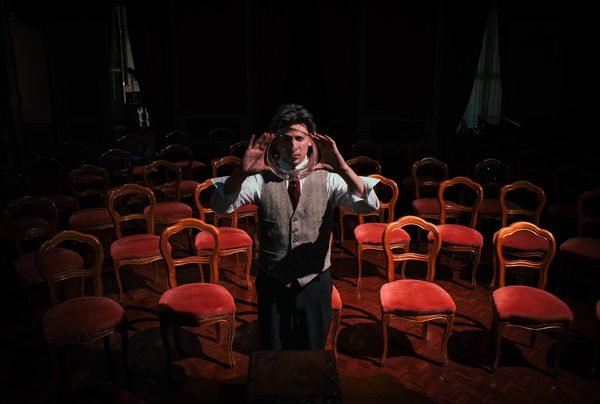 Un illusionista tiene una sfera di vetro davanti al volto, in una sala di sedie rosse